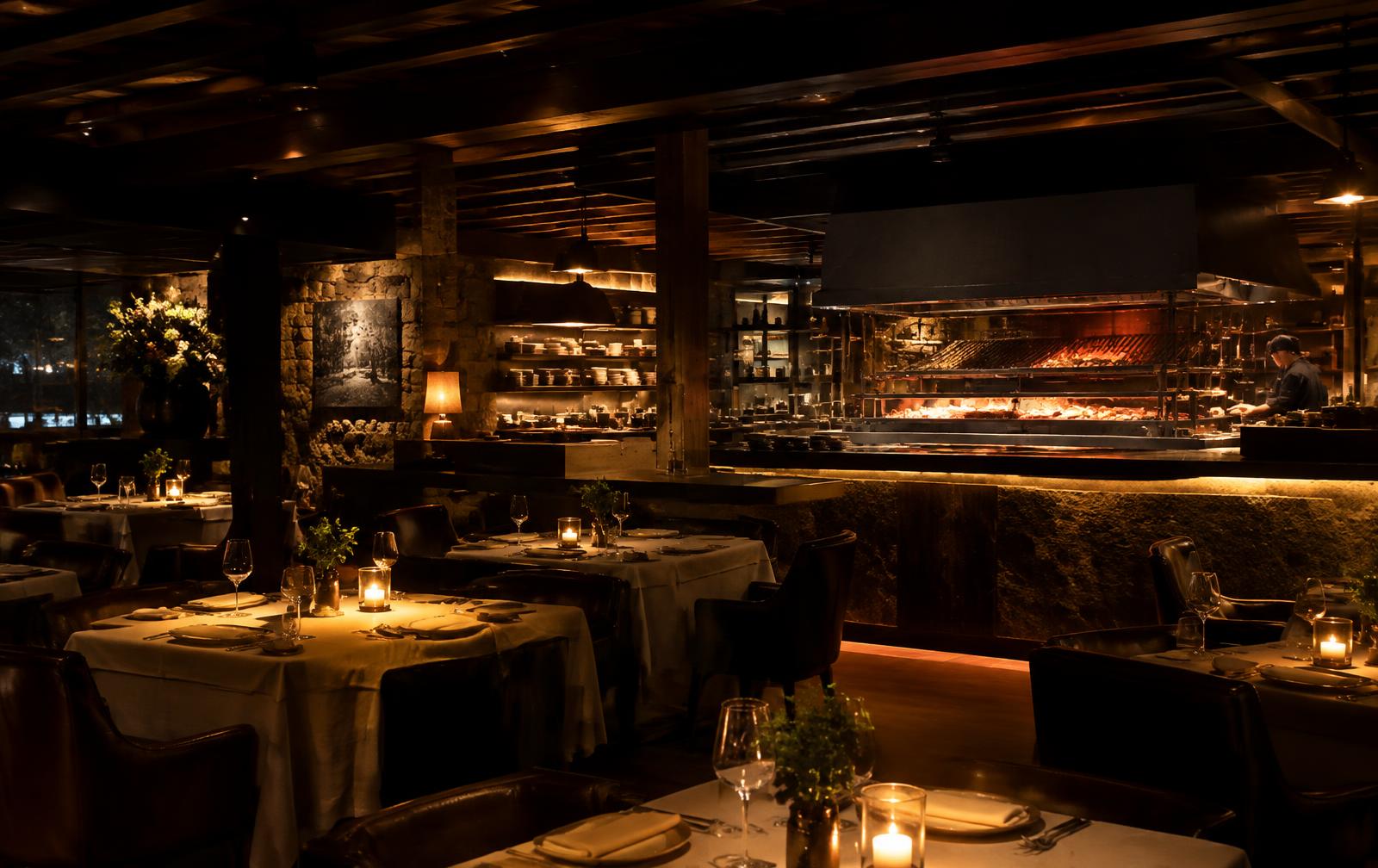 Candlelit dining room with linen-dressed tables and an open charcoal kitchen
